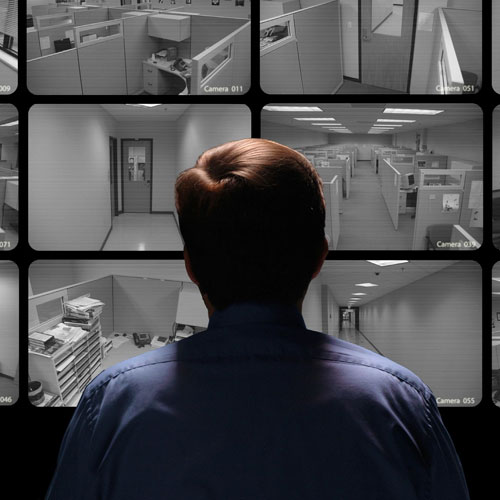 A man looking at multiple monitors in a room.